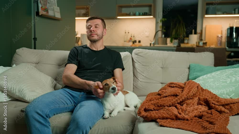 Man sitting on sofa, playing with his dog. Casual man petting dog on couch in living room, enjoying time with pet at home. Concept of relaxation and pet care. Man sitting on sofa, playing with his dog. Casual man petting dog on couch in living room, enjoying time with pet at home. Concept of relaxation and pet care.