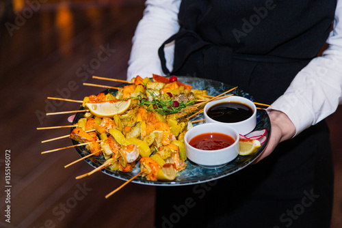Obraz na płótnie Shish kebab from seafood and red fish on wooden skewers on a plate with sauces in the hands of the waiter. overall plan w salonie