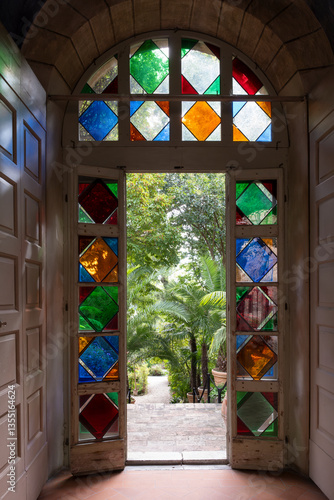 Door with colorful glass elements leading into a Mediterranean botanical garden