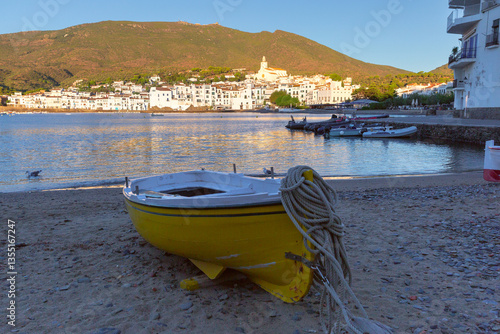 View of fishing boats in the bay of Cadaques in Catalonia, Spain with white buildings and church at sunset