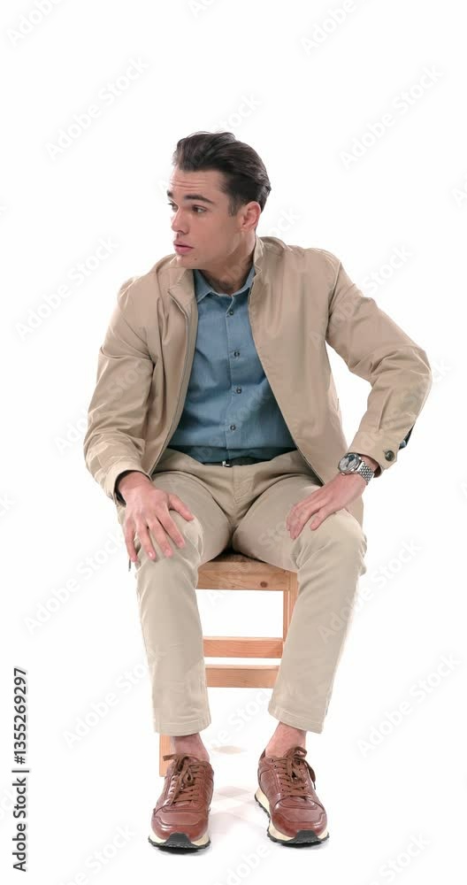 concerned young man sitting, looking to side, putting ankle on knee and being worried, scratching head and thinking of ways to solve difficult problems in front of white background concerned young man sitting, looking to side, putting ankle on knee and being worried, scratching head and thinking of ways to solve difficult problems in front of white background