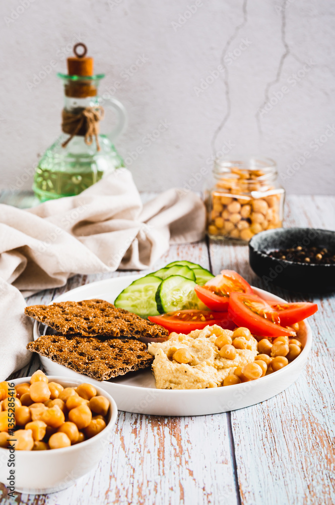 Hummus, chickpeas, tomato, cucumber, grain crackers on a plate on the table vertical view