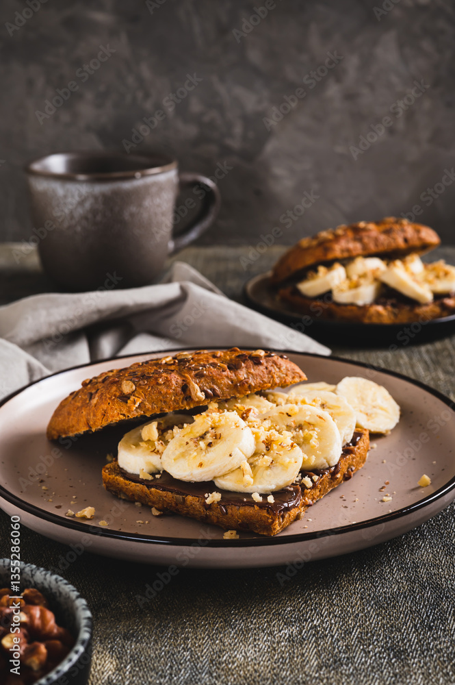 Sweet sandwich with chocolate butter, banana and nuts on a plate on the table vertical view