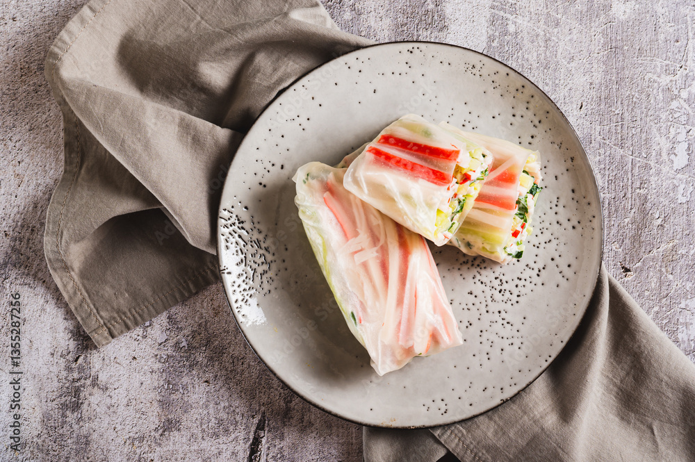 Close up of spring rolls in rice paper with crab sticks, cucumber, greens and sauce on on top view