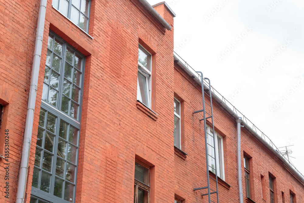 Obraz premium The facade of the old red brick building that was built 100 years ago against the backdrop of the White Sky. Ancient decoration of the building. Restoration of buildings. Old details
