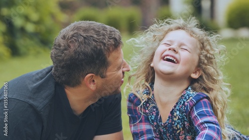 Father laughing together with daughter during sunny park walk, enjoying playful bonding moment with genuine family happiness