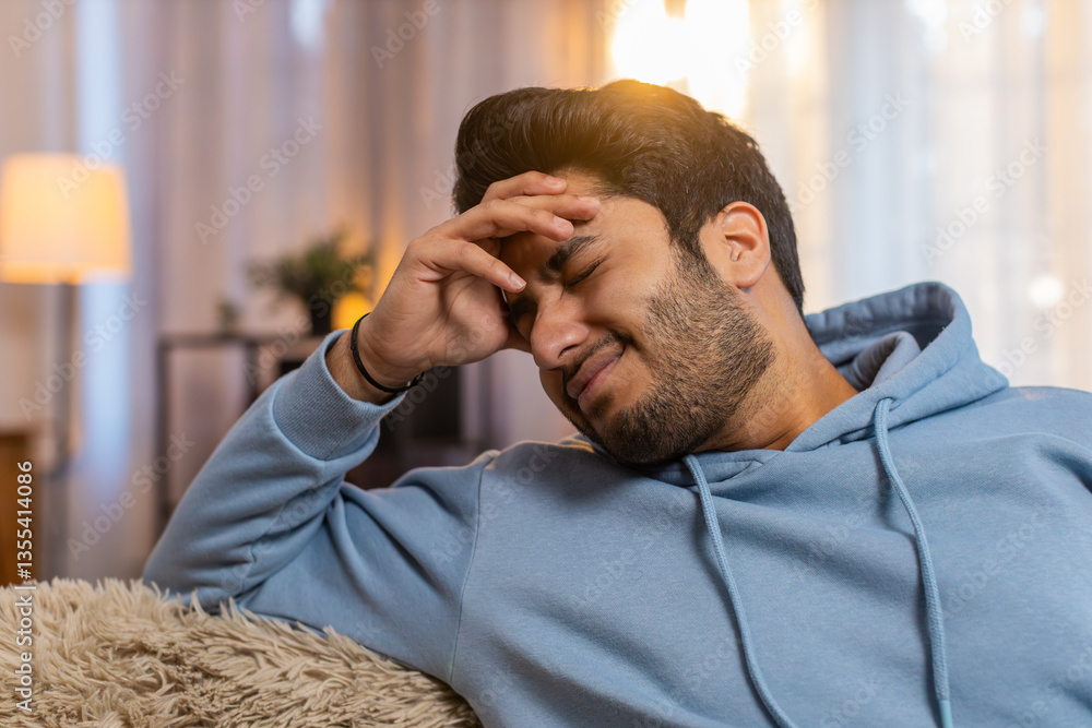 Sick Indian man rubbing temples to cure headache, suffering from tension, migraine, stress, and high blood pressure at home. Hispanic guy holds head, grimacing in pain, experiencing severe discomfort. Sick Indian man rubbing temples to cure headache, suffering from tension, migraine, stress, and high blood pressure at home. Hispanic guy holds head, grimacing in pain, experiencing severe discomfort.