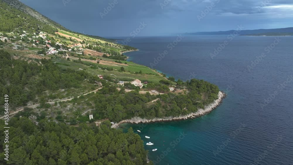 AERIAL: Island village nestled between lush green hills and turquoise blue cove. Rocky shoreline curves around the bay, and few small boats float on calm Adriatic sea. Scenic Mediterranean summer vibe AERIAL: Island village nestled between lush green hills and turquoise blue cove. Rocky shoreline curves around the bay, and few small boats float on calm Adriatic sea. Scenic Mediterranean summer vibe