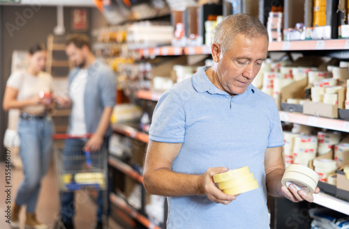 Shopping for various items at a hardware store - elderly male shopper selects double-sided masking tape