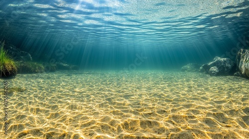 Underwater sunbeams illuminate sandy seabed with rocks and plants.