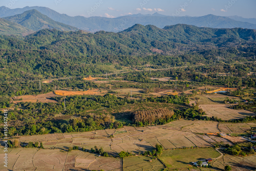 Fototapeta premium Aerial Landscape of Harvested Rice Fields and Lush Green Hills in the Rural Outskirts of Vang Vieng, Laos During Golden Hour