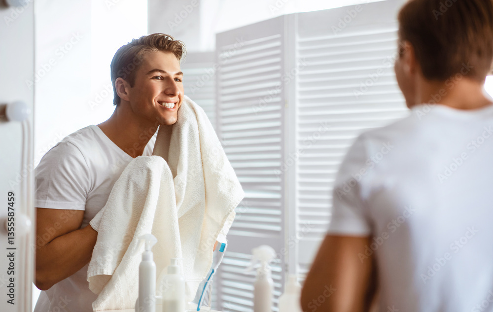 Fototapeta premium Everyday Routine Concept. Good-looking man wiping his face with towel while standing in modern bathroom