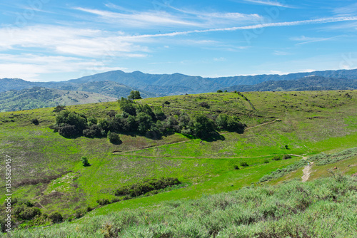 Rolling green hills and scattered trees form the foreground, with winding trails cutting through the landscape, set against distant mountain ranges at Santa Teresa County Park