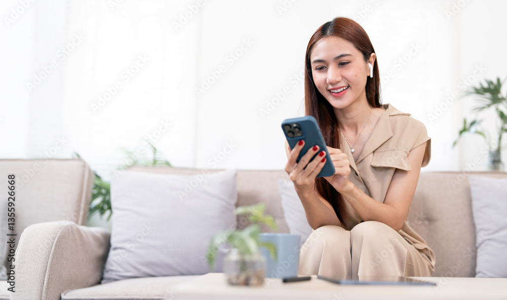 Happy Asian woman using smartphone at home, sits on couch. Work from home Happy Asian woman using smartphone at home, sits on couch. Work from home