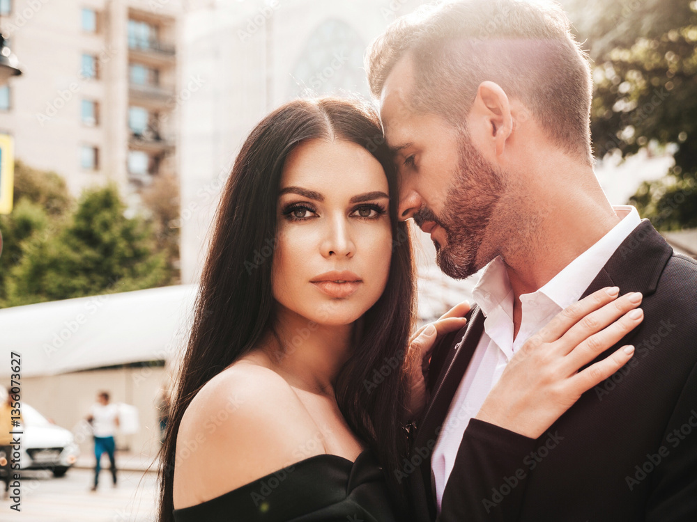 Naklejka premium Beautiful fashion woman and her handsome elegant boyfriend in suit. Sexy brunette model in black evening dress. Fashionable couple posing in the street in Europe. Brutal man and his female outdoors