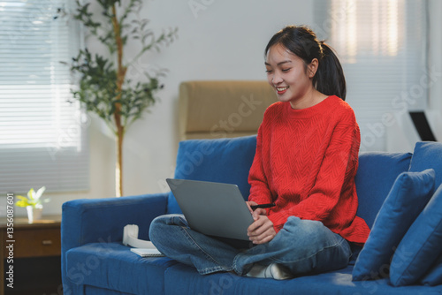 Smiling young asian woman working remotely from home, sitting comfortably on a blue sofa in her living room, enjoying the cozy atmosphere while using her laptop Free Download Smiling young asian woman working remotely from home, sitting comfortably on a blue sofa in her living room, enjoying the cozy atmosphere while using her laptop - GFXLoad