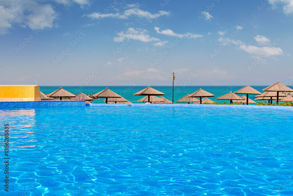 Luxury hotel pool in Sharjah with crystal-clear water, surrounded by elegant sun loungers. Stunning sea views and a golden sandy beach create a relaxing atmosphere under the bright daytime sun.