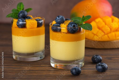 Vegan Italian panna cotta dessert of mango, coconut cream, agar agar and blueberries in glasses on a brown table. Sugar, lactose and sugar substitutes free.