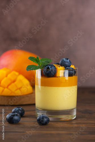 Mango panna cotta mousse pudding with blueberries and mint leaf on a brown wooden table. Vegan food, sugar, lactose and sugar substitutes free. Vertical orientation.
