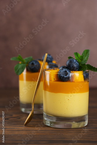 Vegan mango panna cotta mousse pudding with blueberries with golden spoon on a wooden table. Sugar, lactose and sugar substitutes free. Vertical orientation.