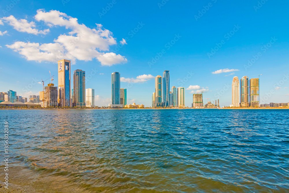 Sharjah city skyline at sunrise with golden light reflecting on modern skyscrapers. Serene beach with gentle waves. Peaceful morning atmosphere in the UAE’s cultural capital.