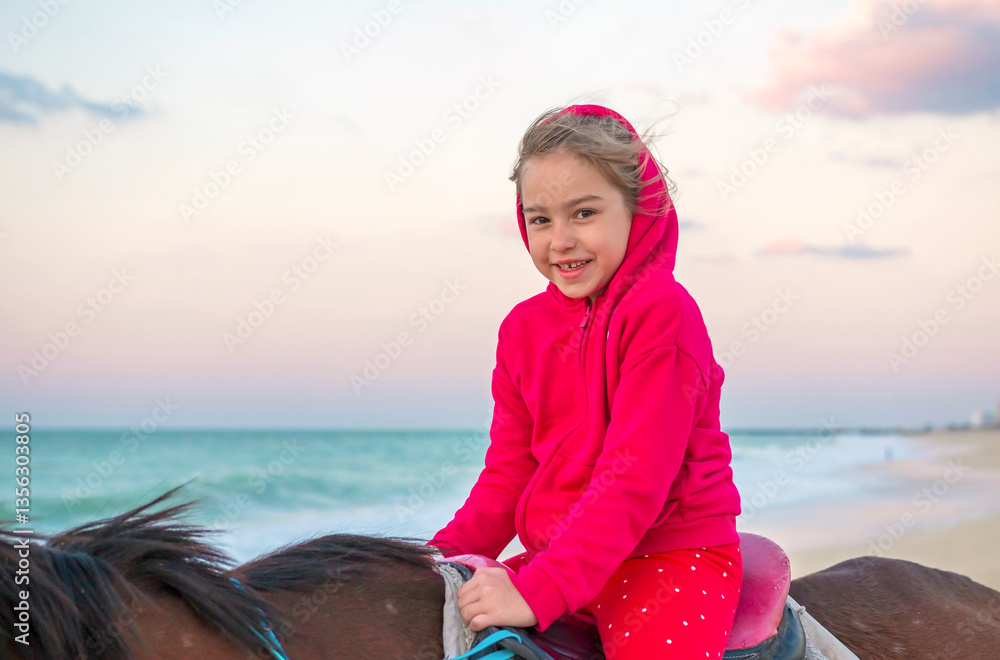 A joyful girl smiling while riding a horse on the beach in Sharjah at sunset. The warm golden light of the setting sun reflects on the water, creating a serene and magical moment