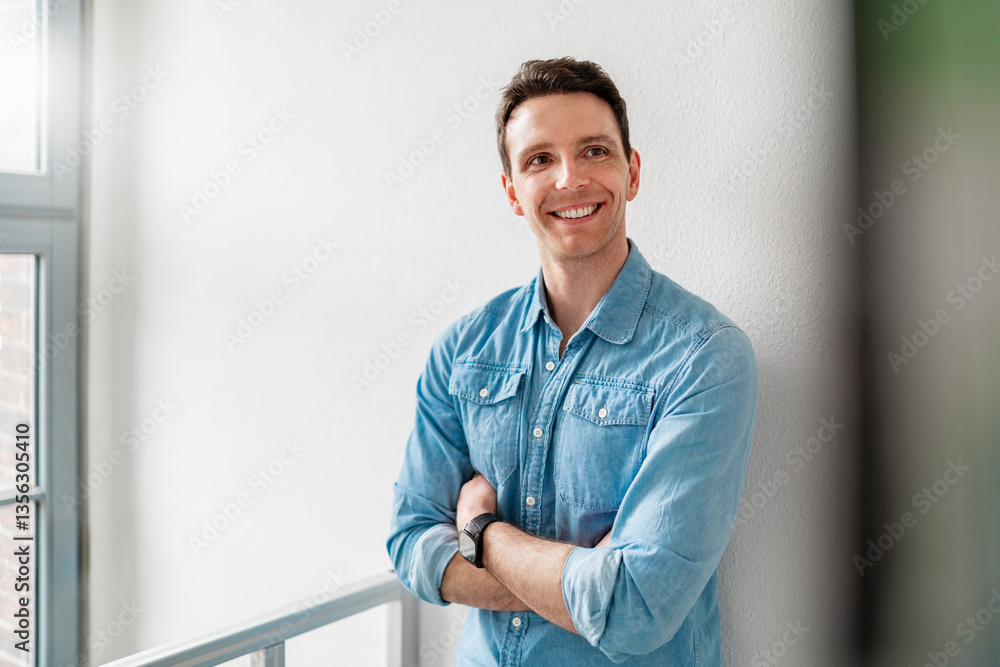 Young man in a denim shirt smiling confidently in an office setting Young man in a denim shirt smiling confidently in an office setting