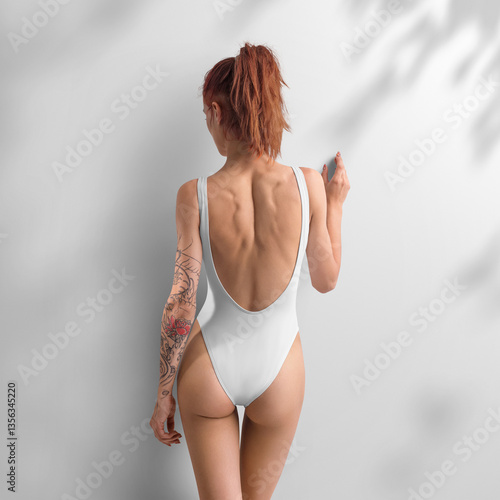 Template of white monokini on slim redhead girl with tattoo, swimsuit with open back, back view, on natural shadows background.