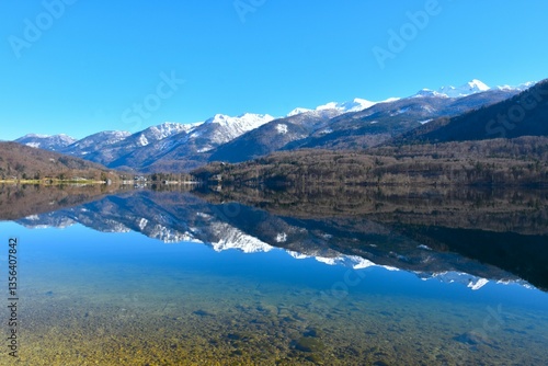 View of snow covered mountain peaks in Julian alps and lake Bohinj bellow with a reflection of the mountains on the water in Gorenjska, Slovenia