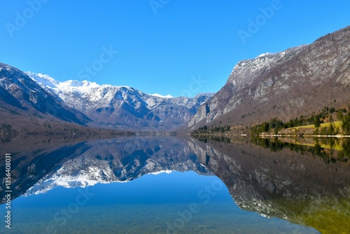 View of lake Bohinj and mountain above covered in snow and a reflection of the mountains in the water in Gorenjska, Slovenia