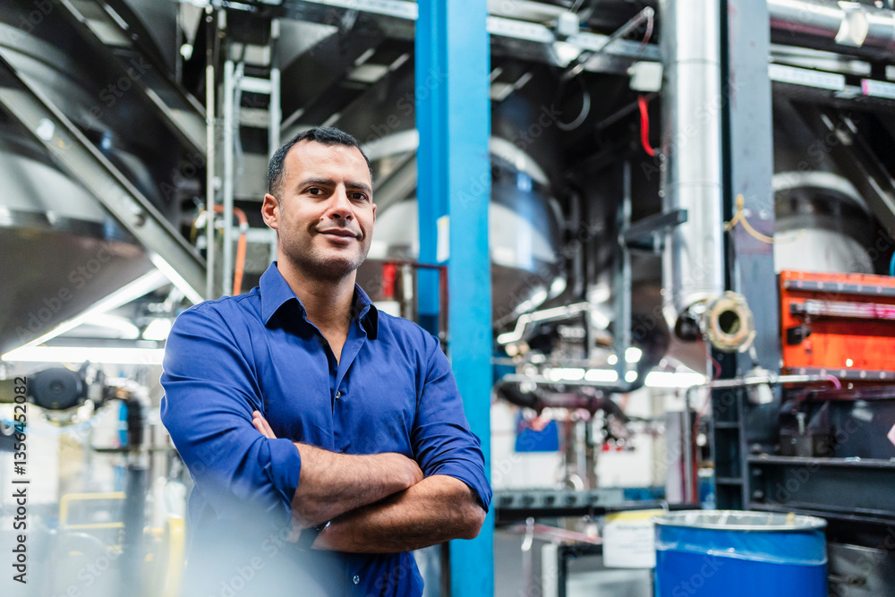 Mature manager with arms crossed standing in factory Mature manager with arms crossed standing in factory