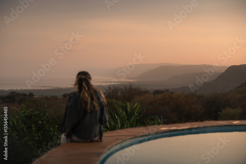 Tourist contemplating sunset over lake manyara from a lodge with swimming pool during a safari trip in tanzania, africa