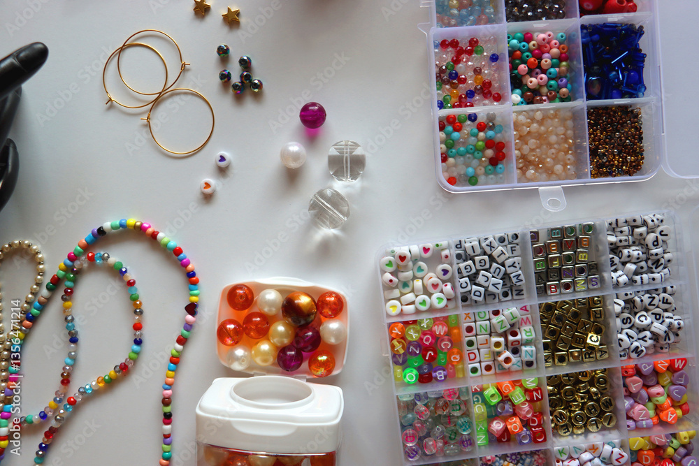 Hand figurine, colorful friendship bracelets, necklaces, various beads and DIY supplies on the table. Making jewelry at home. Flat lay.