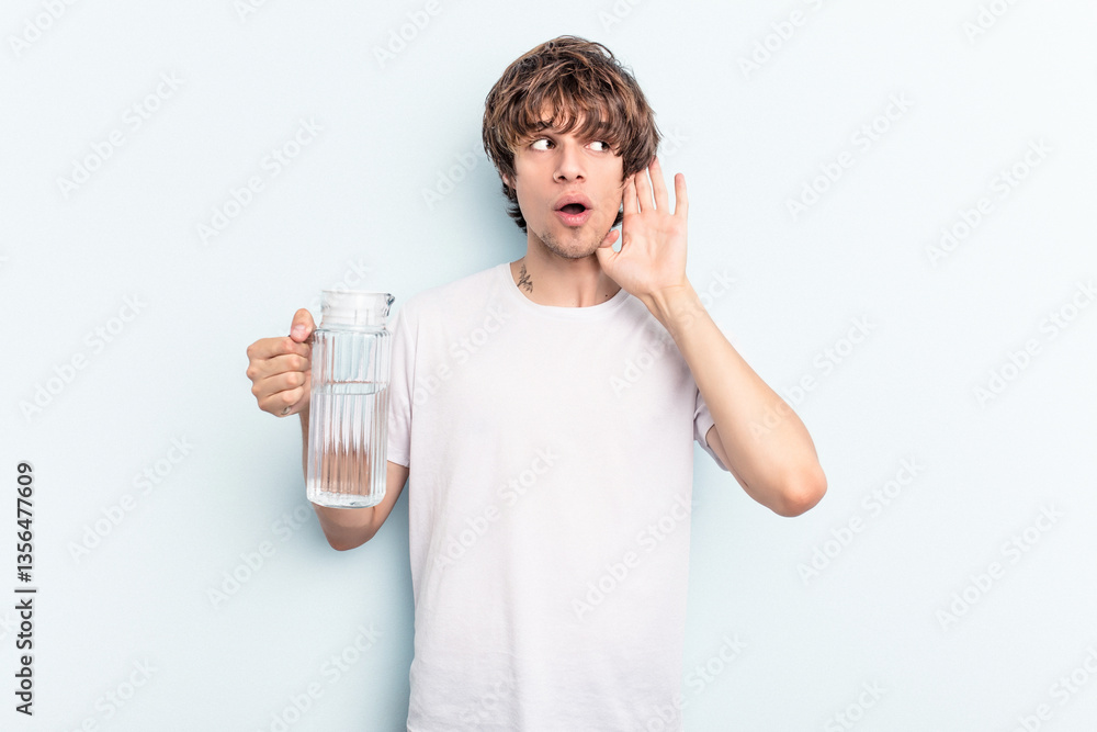 Young caucasian man holding a jar of water isolated on blue background trying to listening a gossip. Young caucasian man holding a jar of water isolated on blue background trying to listening a gossip.