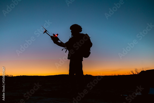 Silhouettes of soldiers are using drone for scouting during military operation against the backdrop of a sunset.