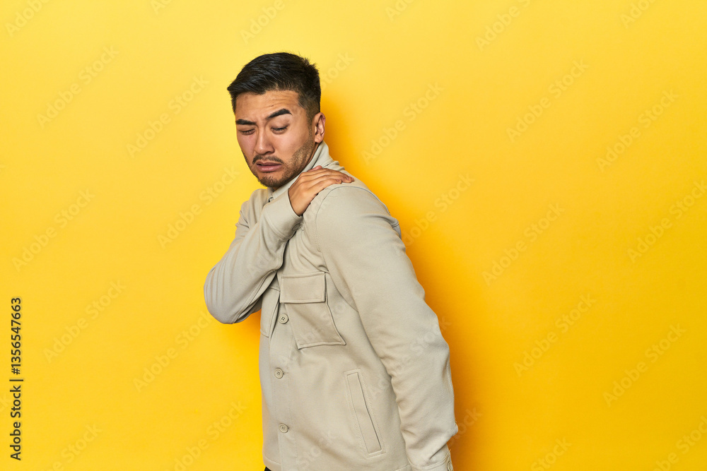 Fototapeta premium Asian man in stylish gray shirt on yellow studio having a shoulder pain.