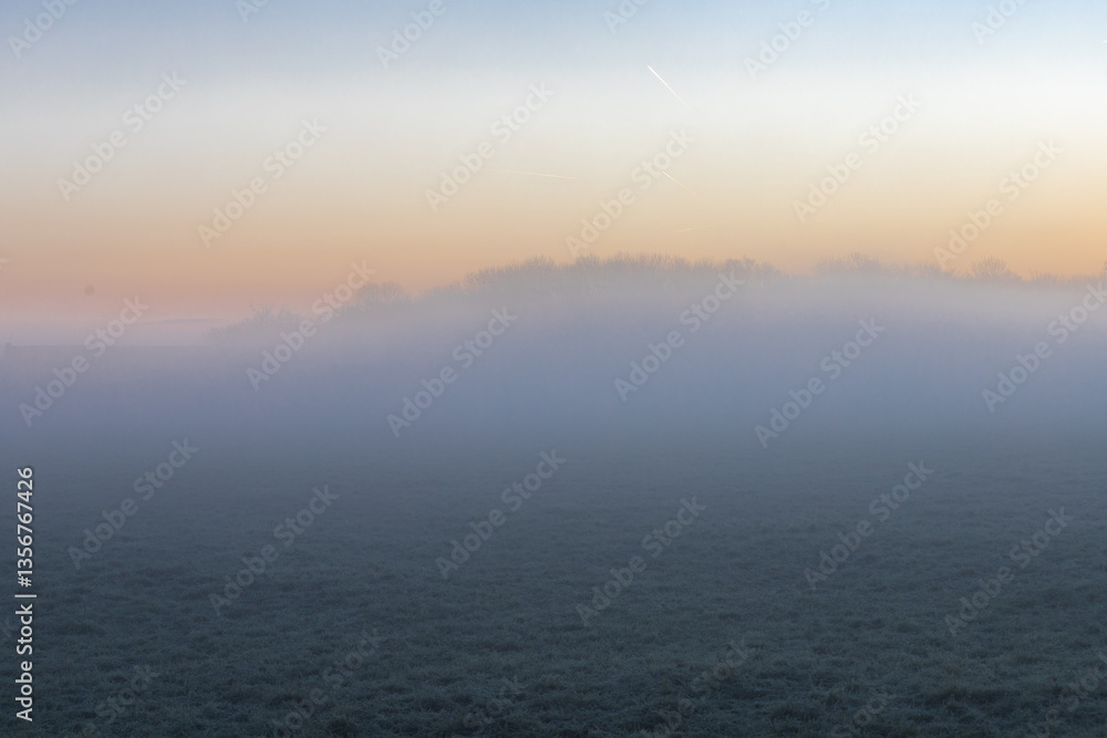 Obraz premium Sunrise over the rolling hills of the sint Pietersberg in Maastricht on a misty December morning, creating a fairy like landscape with the sun peaking through the fog