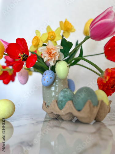 An Easter card. Colorful bright tulips decorated with eggs are in a vase on the table next to colorful eggs. Vertical photography