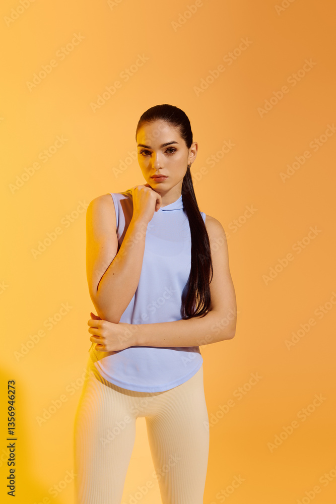Naklejka premium Confident young woman poses against a bright orange backdrop, showcasing her athleticism