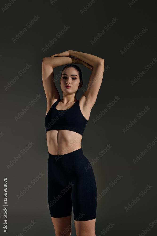 Fototapeta premium Sporty woman stretching in a stylish black outfit against a dark background