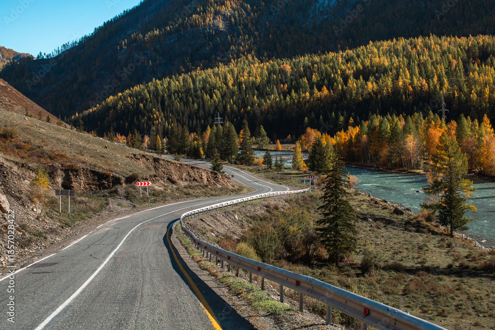 A zigzagging road through the Altai Republic with a river flowing on the right, surrounded by rugged mountains and lush wilderness.