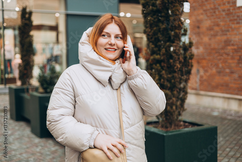 Obraz na płótnie Happy 30s woman talking phone and look happy outdoors. Urban lifestyle concept. Winter time. Beautiful redhead woman walking on the city street. w salonie