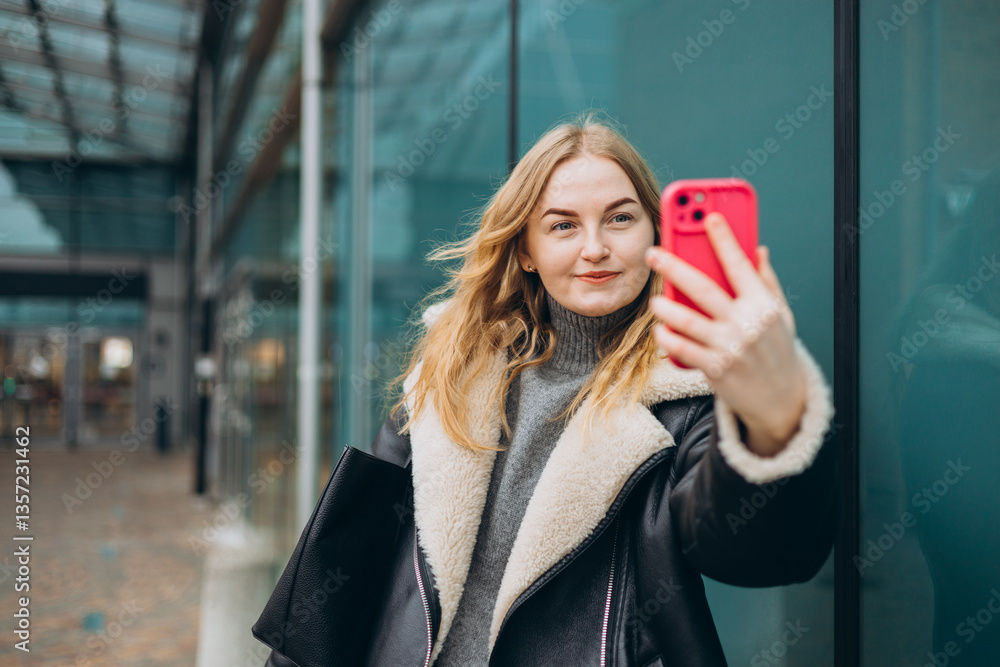 Happy blonde Woman makes selfie mobile photo on modern urban background. Charming female wearing stylish outfit have fine. High quality photo.