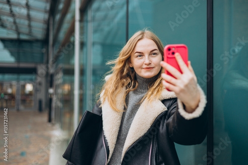 Obraz na płótnie Happy blonde Woman makes selfie mobile photo on modern urban background. Charming female wearing stylish outfit have fine. High quality photo. w salonie