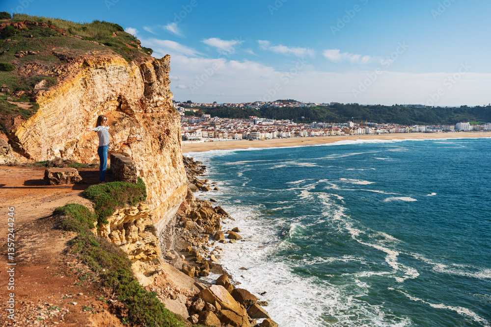 Woman standing on the rocky cliffs of Nazare at the western Atlantic coast of Portugal