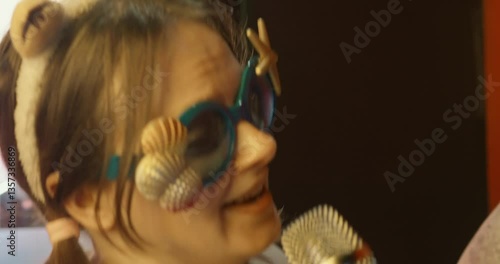 Woman wearing whimsical seashell adorned sunglasses belting out song passionately during lively karaoke event, radiating exuberant musical energy
