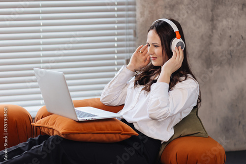 Smiling Woman in Headphones Working on Laptop from Cozy Couch at Home