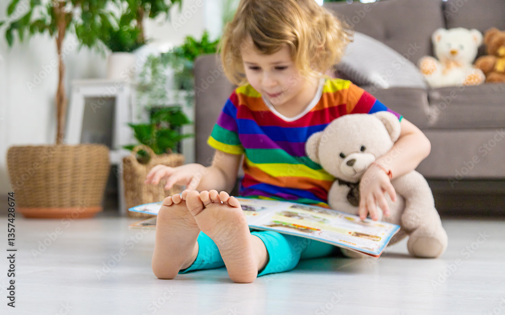 Child reading a book at home with a teddy bear at home. Selective focus. Child reading a book at home with a teddy bear at home. Selective focus.
