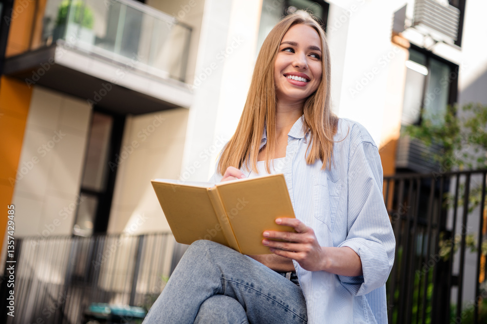 Charming young woman reading a book outdoors in urban setting on a sunny day, enjoying leisure time with a cheerful smile. Charming young woman reading a book outdoors in urban setting on a sunny day, enjoying leisure time with a cheerful smile.