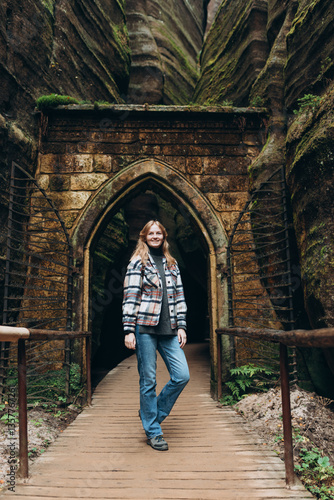 Obraz na płótnie A tourist woman with a backpack stands against the background of a rocks. Young 30s blonde woman hiking in nature. Concept of an active lifestyle. High quality photo. Full body w salonie